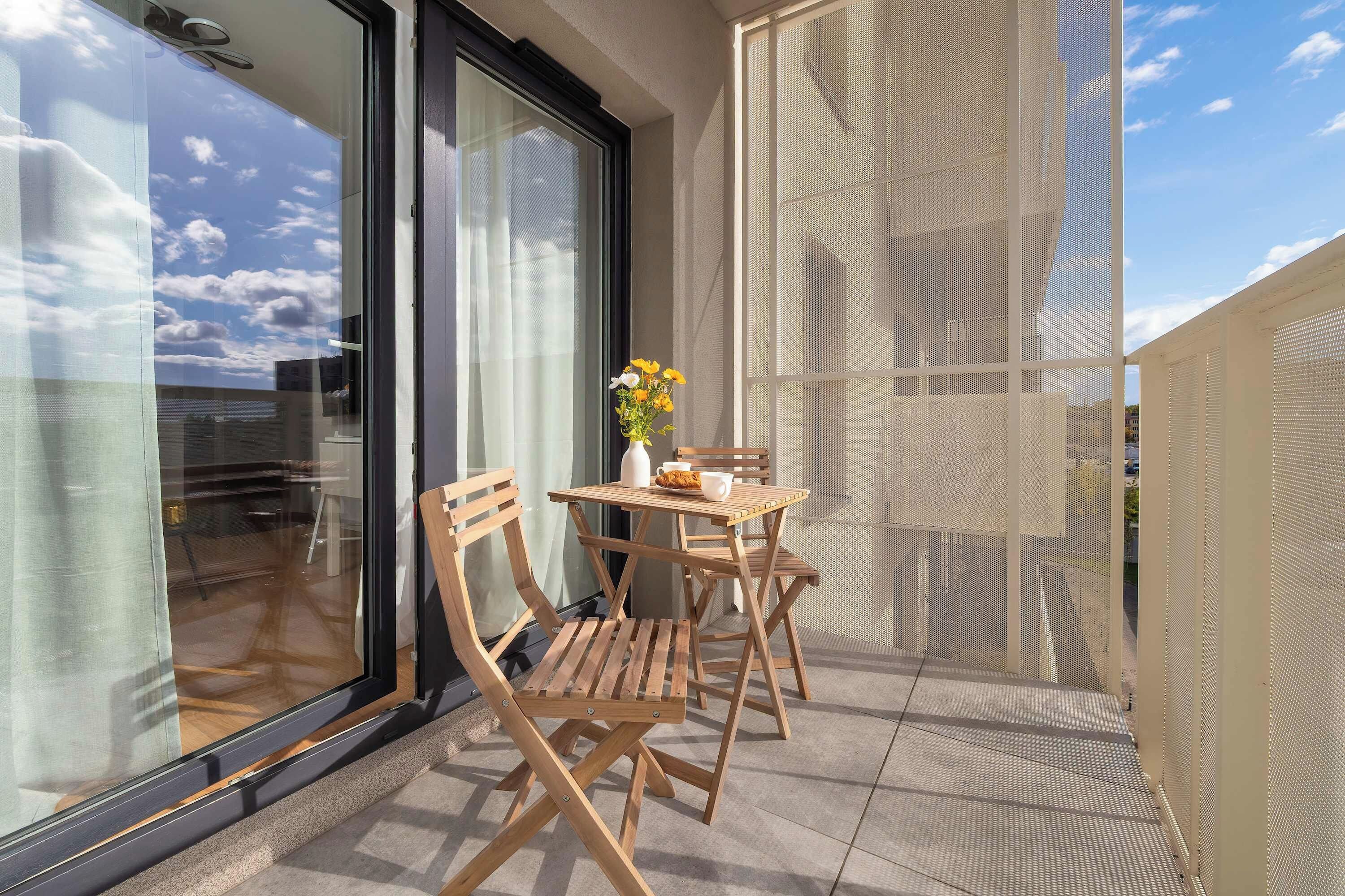 En balkon med et bord, stole og en blomstervase.