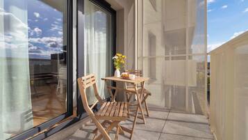 En balkon med et bord, stole og en blomstervase.