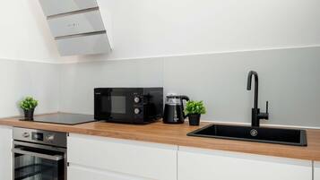 Een moderne keuken met een inbouwoven, een magnetron, een waterkoker en een zwarte kraan.