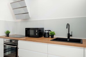 Een moderne keuken met een inbouwoven, een magnetron, een waterkoker en een zwarte kraan.