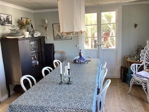 A dining area with a patterned tablecloth, white chairs, a cabinet with glassware, and a door leading outside. - 8 Person Holiday Home in Bovallstrand (Bovallstrand)