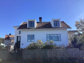 A two-story house with a white exterior, a tiled roof, and a wooden fence in the foreground. - 8 Person Holiday Home in Bovallstrand (Bovallstrand)