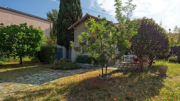 Una propietat residencial amb un camí de pedra que condueix a una casa, envoltada de vegetació i sota un cel serè.
