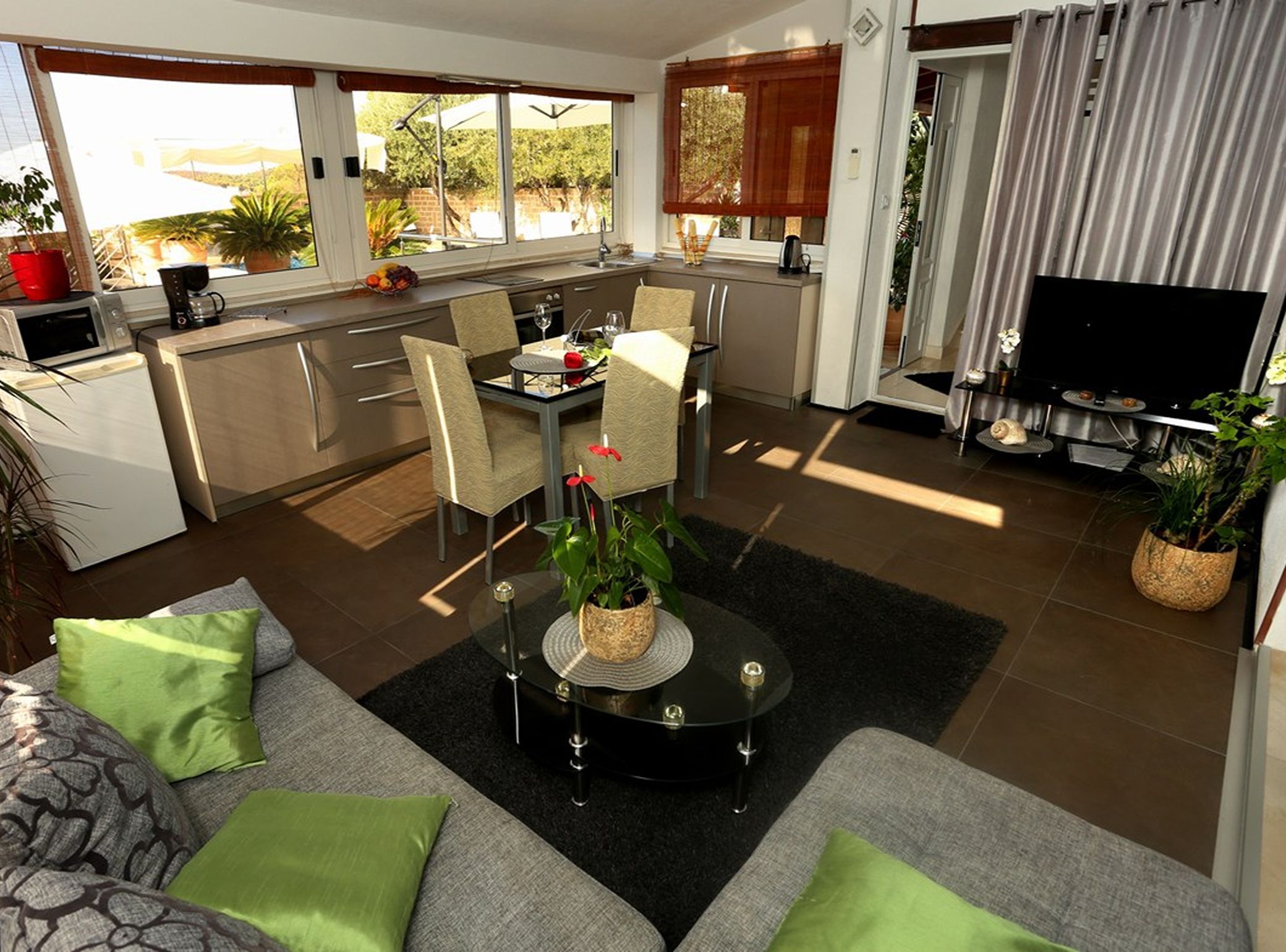 Una sala moderna con un sofá, una mesa de comedor y sillas. Hay una zona de cocina con una cafetera y un televisor.