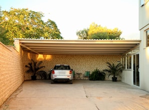 A covered parking area with a car parked inside, a brick wall, and potted plants. - Apartments Villa Di (Okrug)