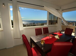 A dining area with a table set for two, red chairs, and a view of the sea. - Apartments Villa Di (Okrug)