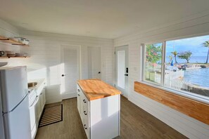 Eine Küche mit weißen Schränken, einer Holz Arbeitsplatte und Blick auf das Meer durch ein großes Fenster.