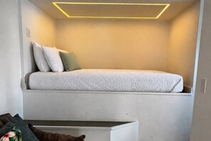 Un lit compact doté d’une tête de lit, d’une table de chevet et d’un luminaire fixé au mur.