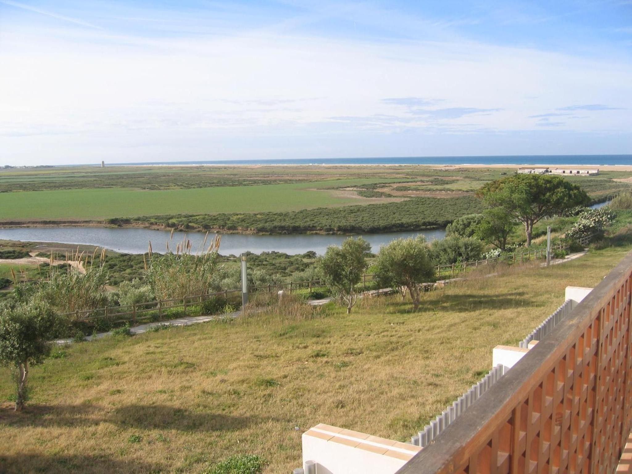 Een overzicht van een kustlandschap met een rivier, grasvelden en een gebouw in de verte.