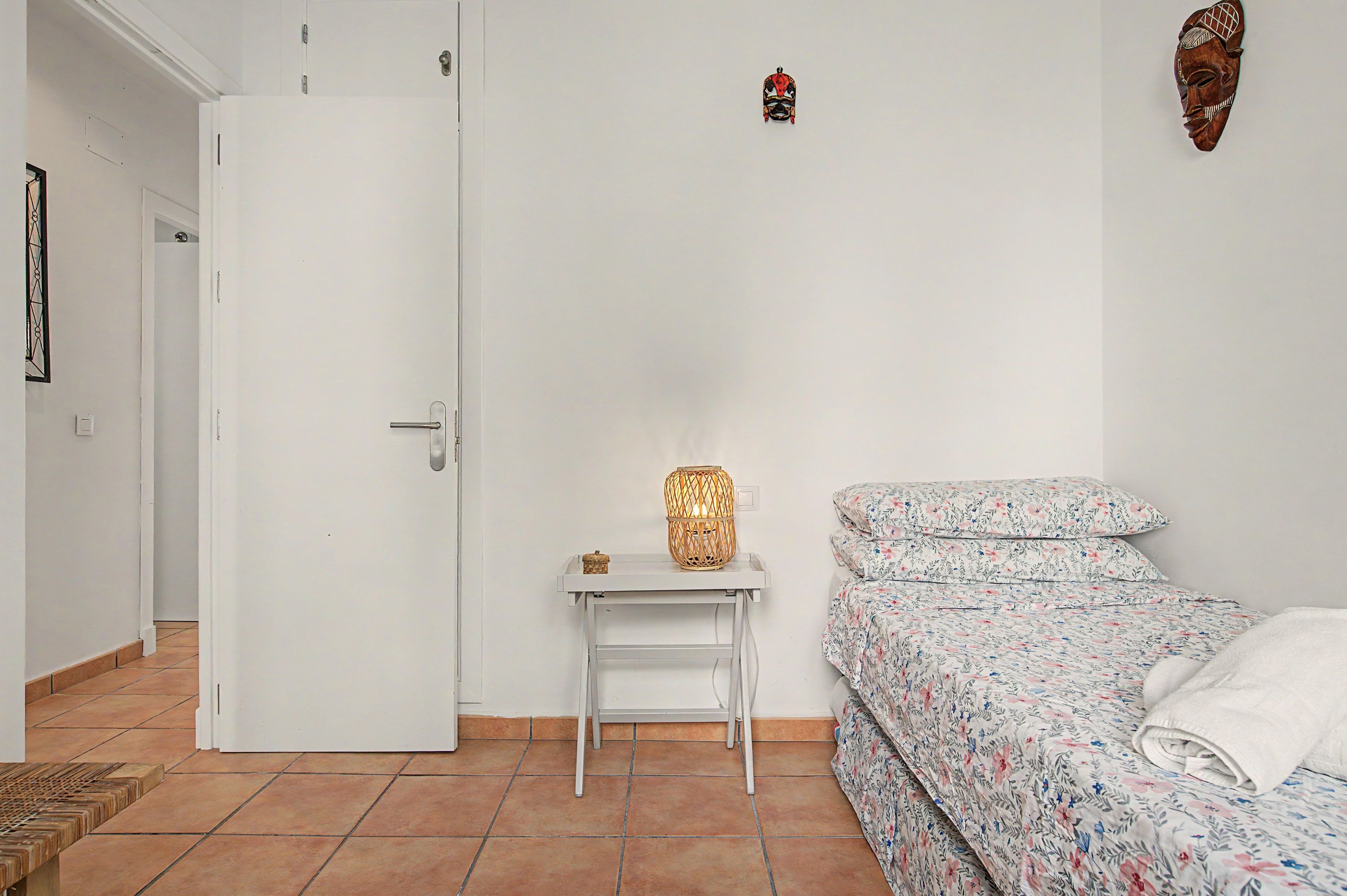 Een slaapkamer met een bed, een nachtkastje met een lamp en een deur.