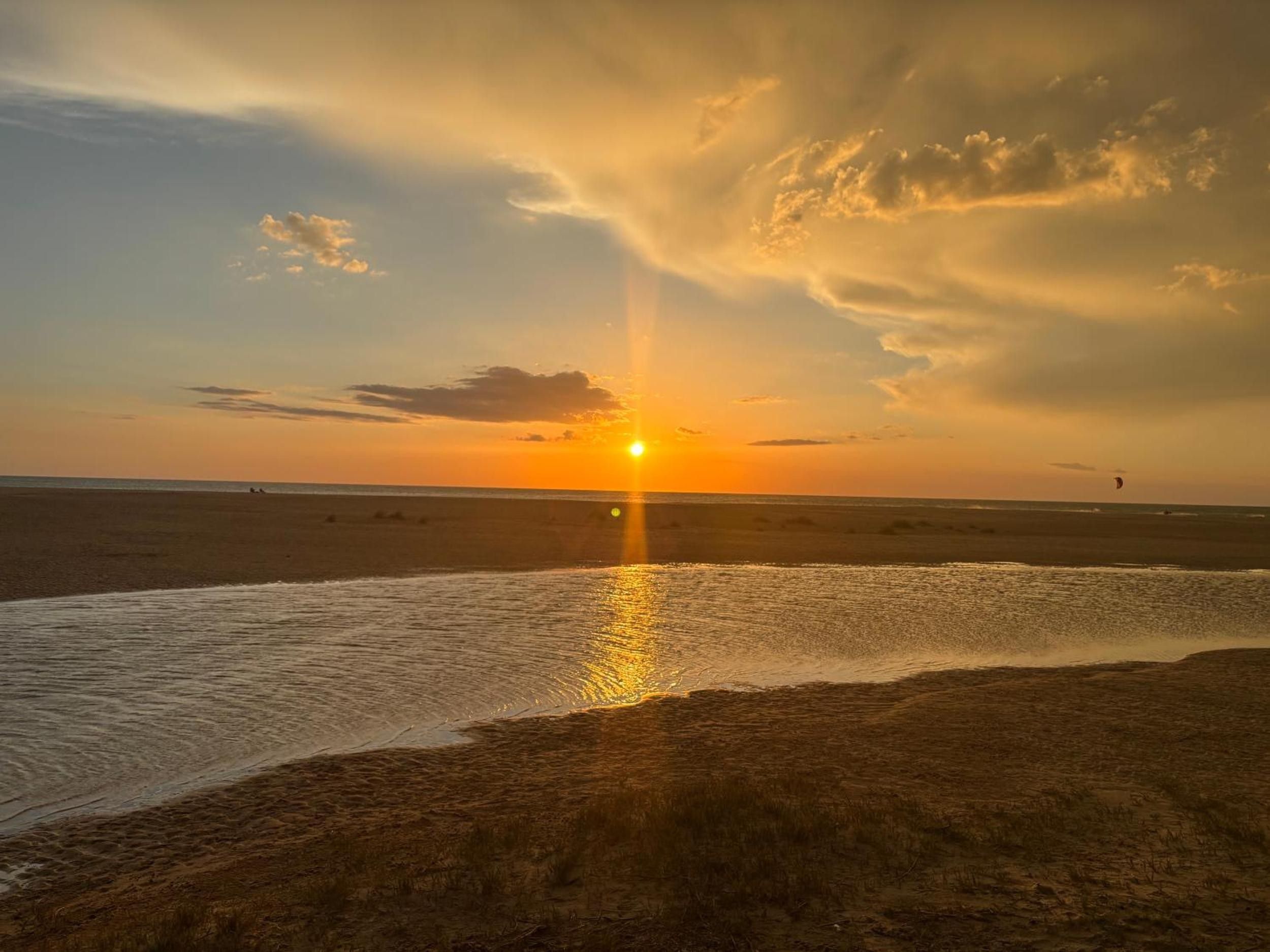 Escena de playa con el sol poniéndose en el horizonte, reflejado en el agua.