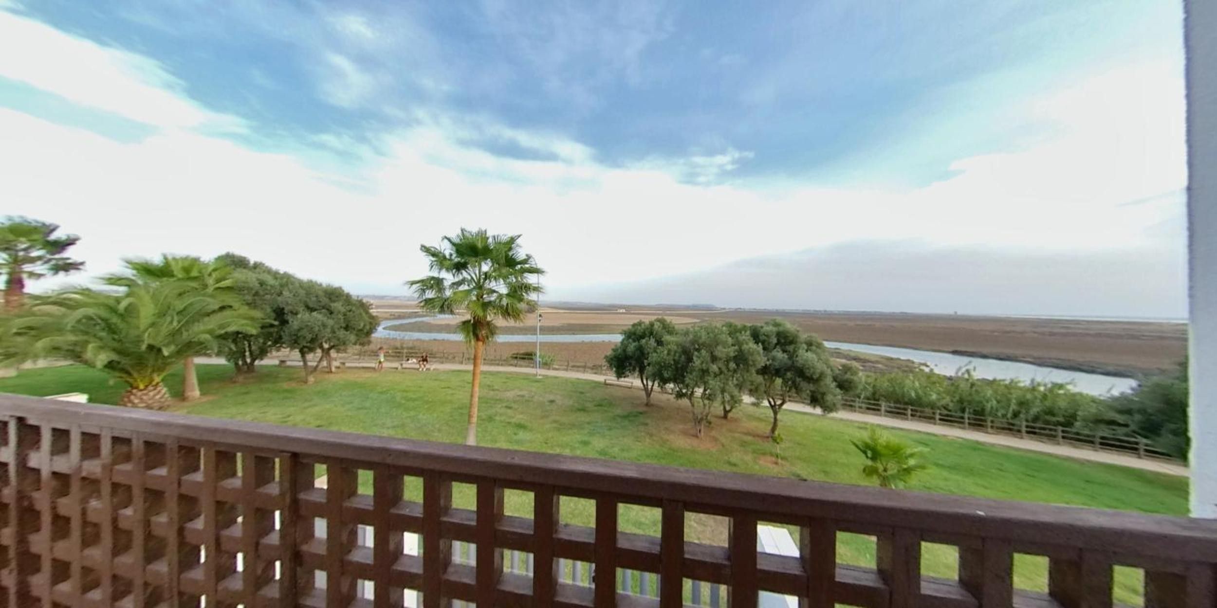 Un balcon donnant sur un espace verdoyant, des arbres et une étendue d’eau.