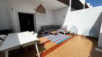 Eine sonnendurchflutete Terrasse mit einem weißen Tisch, einer Couch und zwei Stühlen.