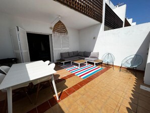 A sunlit patio with a white table, a sofa, and two chairs.