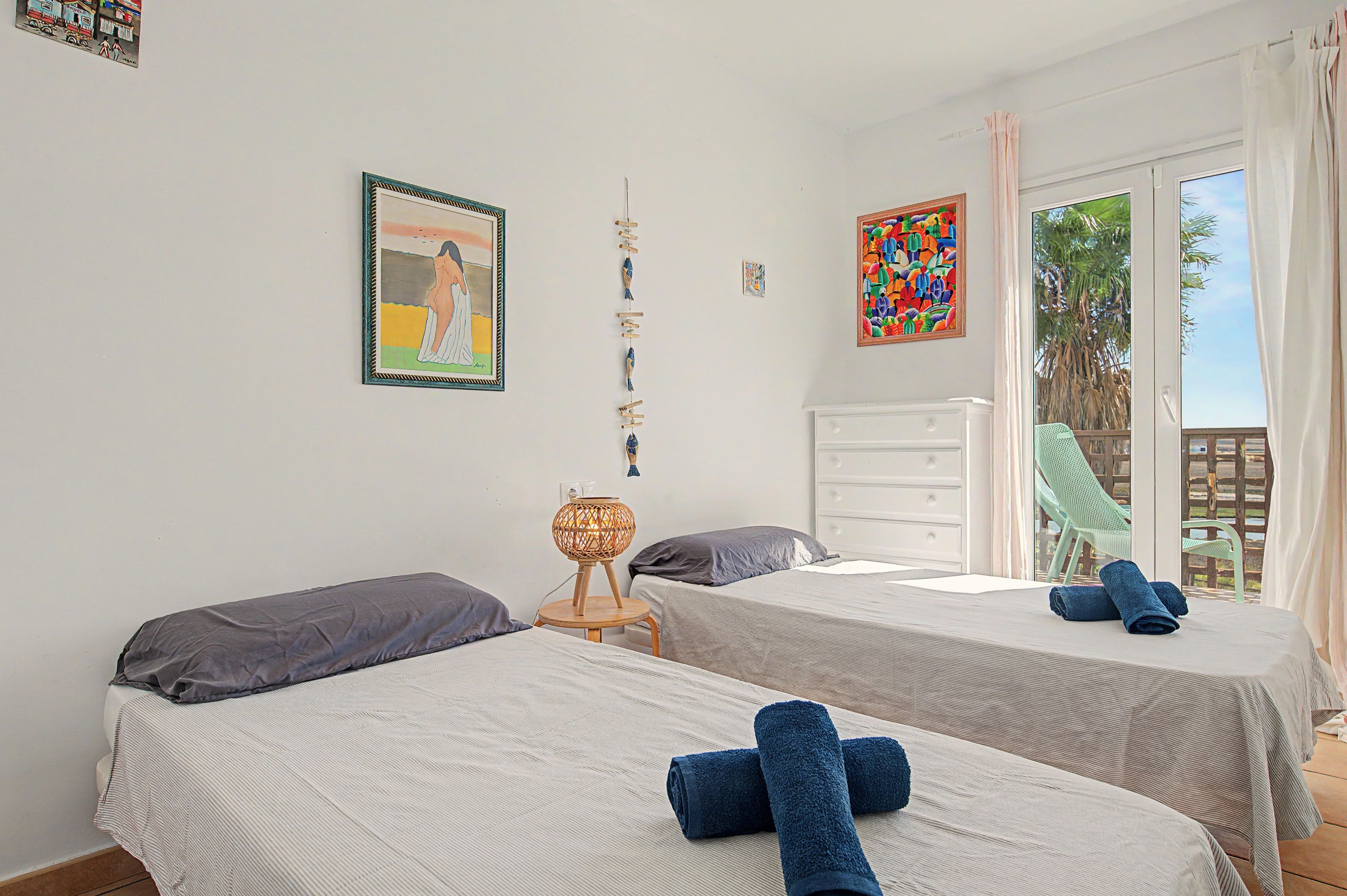Une chambre avec deux lits, une table de chevet, une lampe et une fenêtre donnant sur des palmiers.