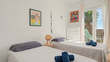 Une chambre avec deux lits, une table de chevet, une lampe et une fenêtre donnant sur des palmiers.