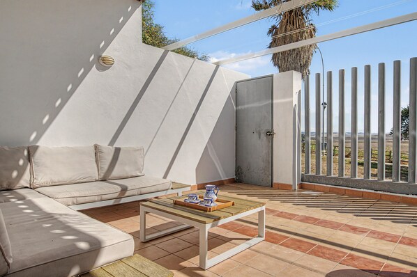 Un área de estar moderna al aire libre con un sofá y una mesa de centro, una reja de metal y vistas al paisaje.