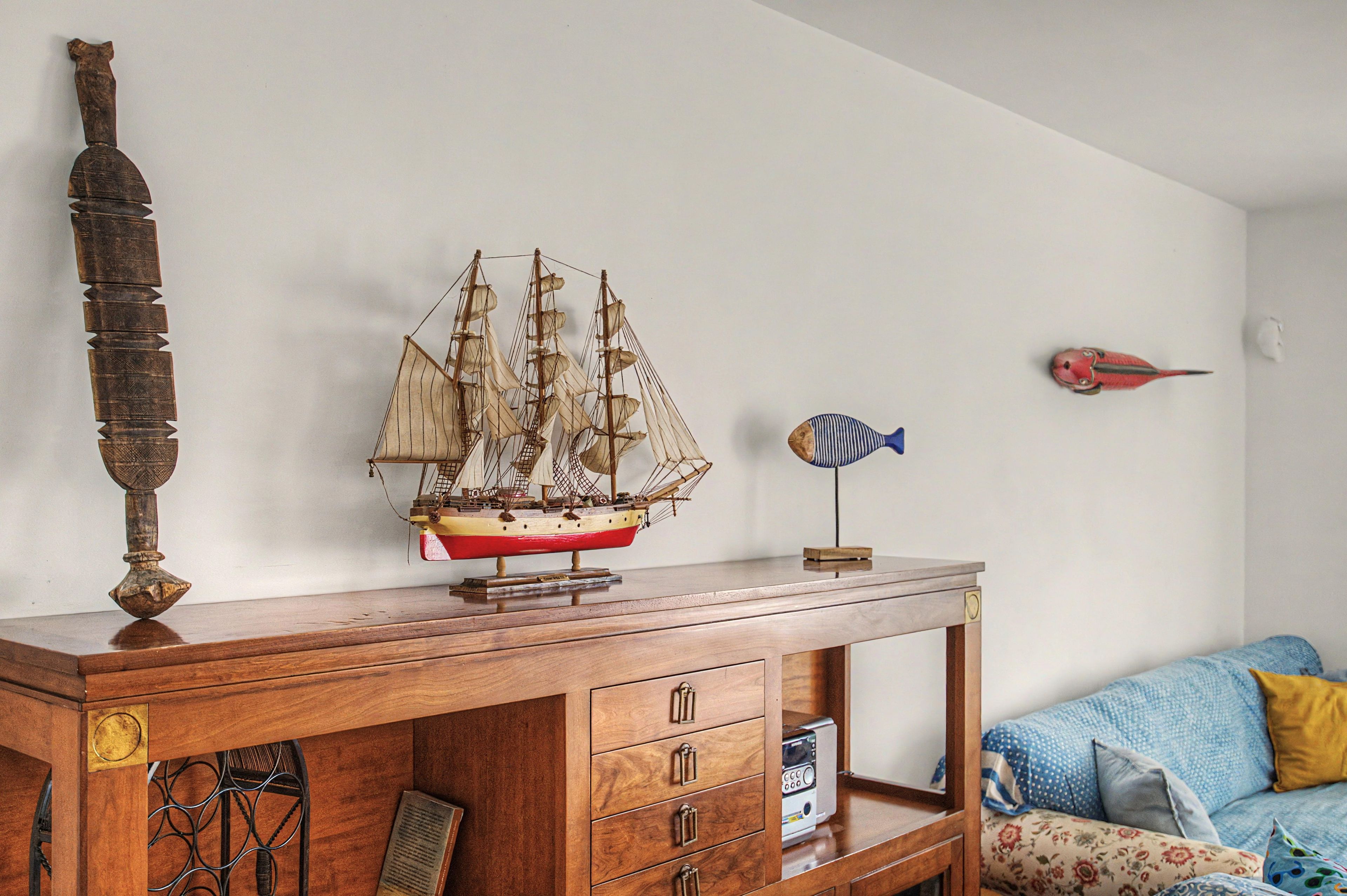 A wooden cabinet with drawers, a ship model, a fish model, and a decorative item on the wall.