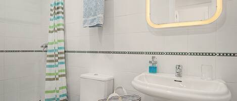 A bathroom with a shower, toilet, sink, and a mirror.