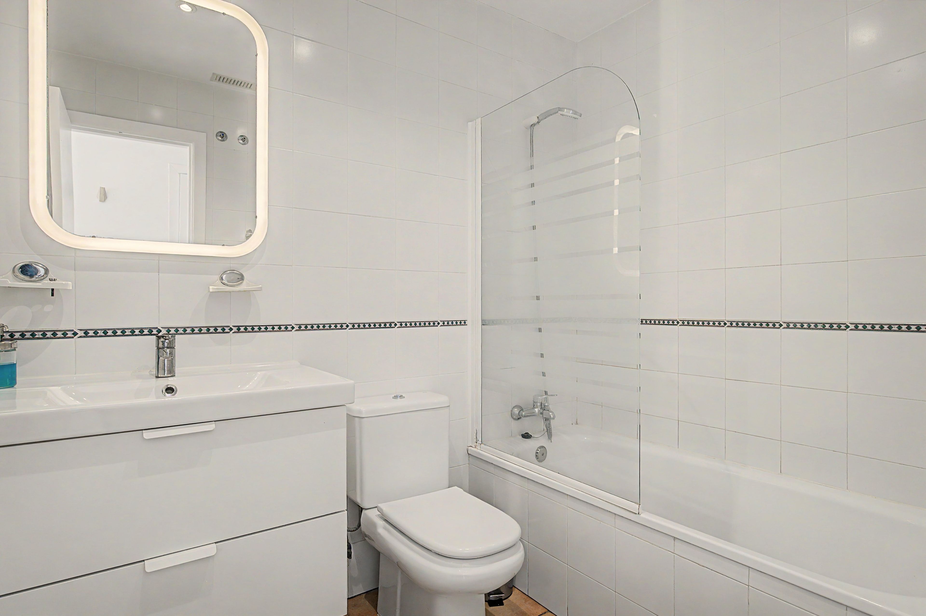 Een badkamer met een wit wastafel, spiegel, toilet en douche.