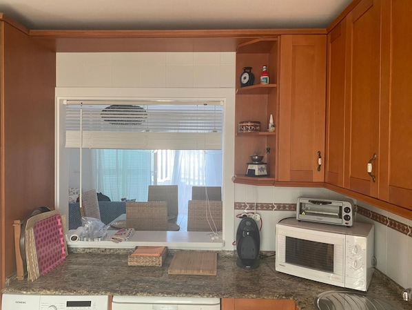 A compact kitchen with a microwave, toaster, and a window with blinds.
