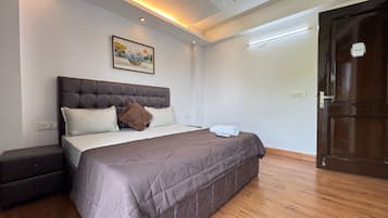 Un dormitorio con una cama grande, ventilador de techo, luces empotradas, un cuadro en la pared y piso de madera.