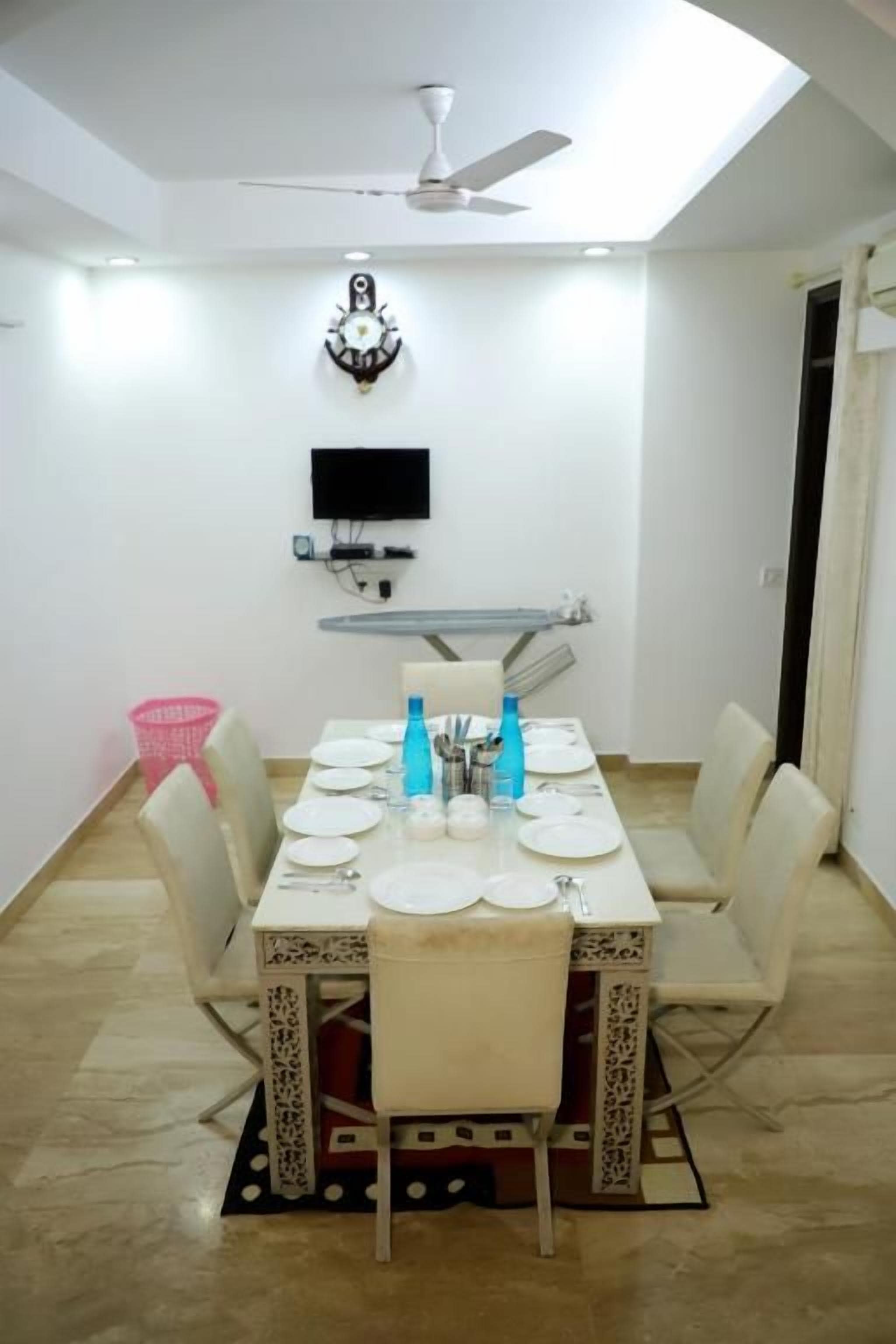 Un coin repas avec une table dressée pour quatre personnes, un ventilateur de plafond, un téléviseur fixé au mur et un luminaire fixé au mur.
