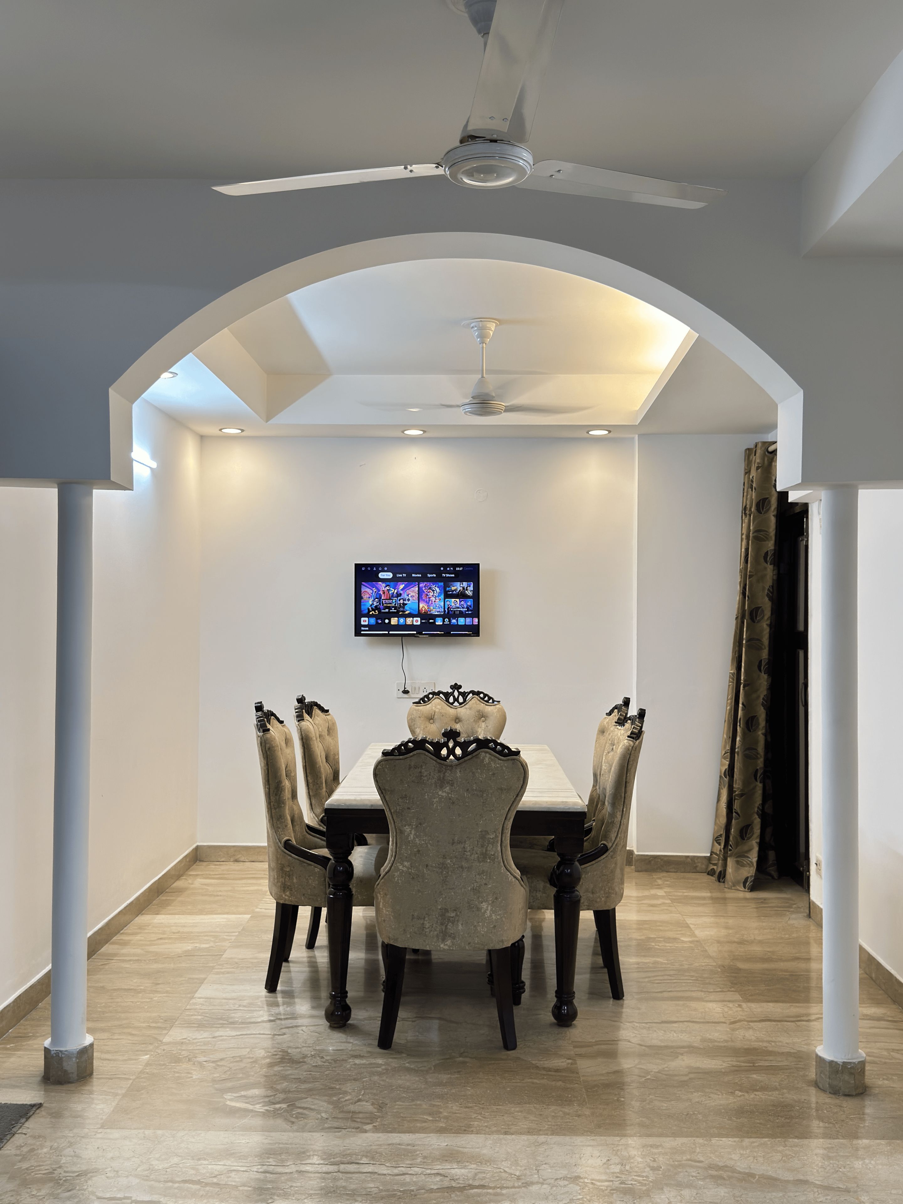 A dining area with a table and chairs, a ceiling fan, recessed lighting, and a flat-screen TV mounted on the wall.