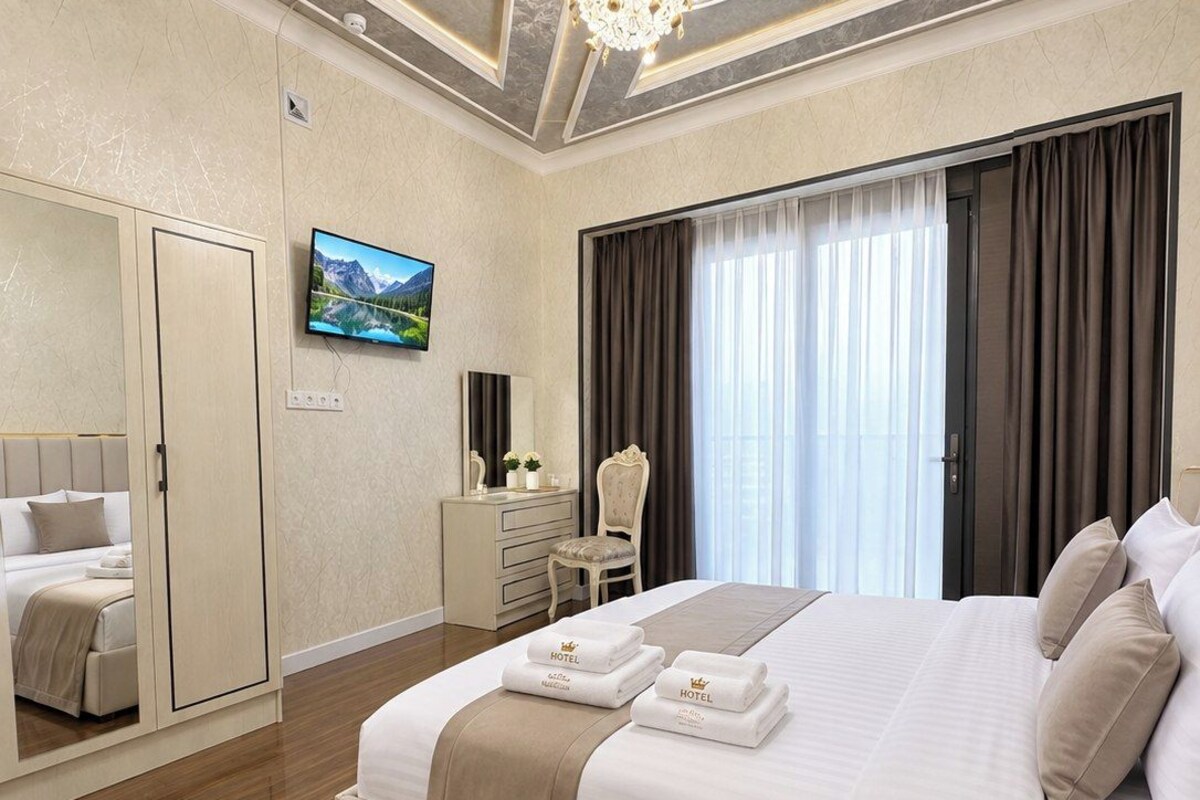 Quarto de hotel com uma cama grande, televisão, guarda-roupa, secretária e um candelabro.