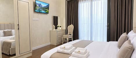 Ein Hotelzimmer mit einem großen Bett, einem Fernseher, einem Kleiderschrank, einem Schreibtisch und einer Kandelaber.