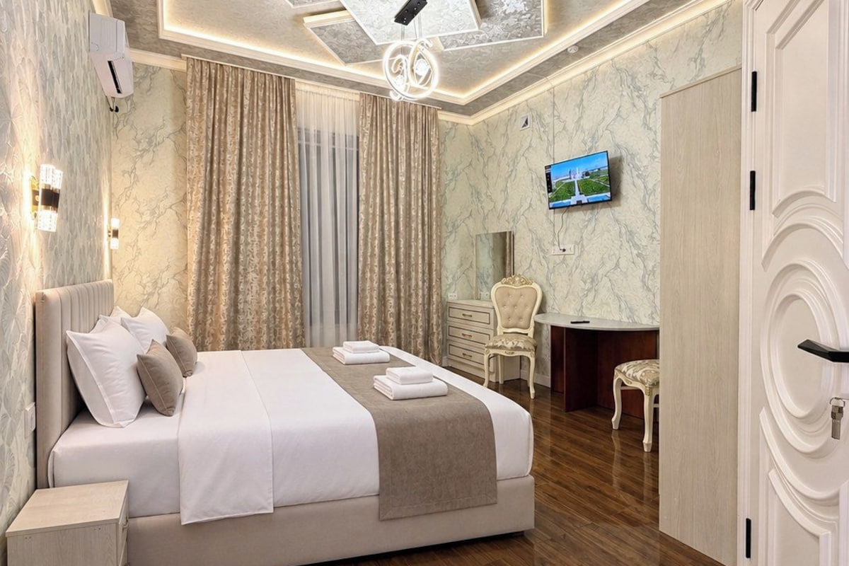 Quarto de hotel moderno com uma cama grande, televisão e piso de madeira.