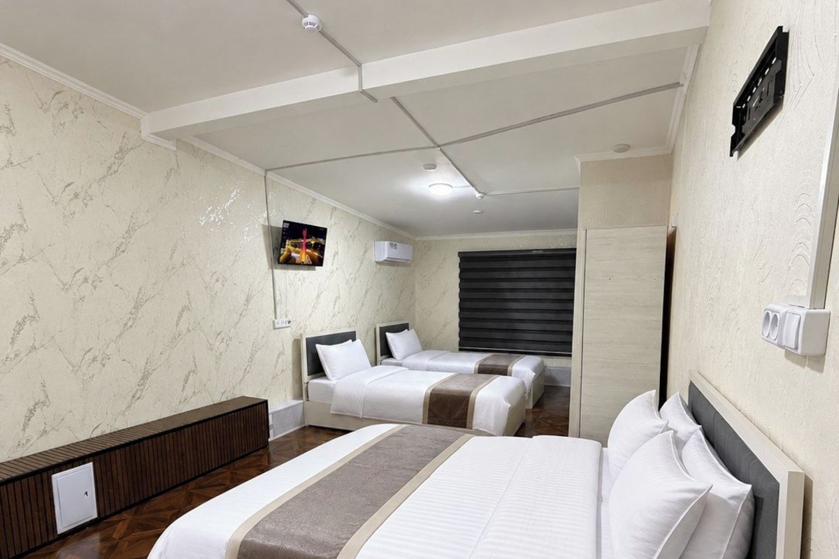 Quarto de hotel com uma cama grande, uma cama menor e um espaço de estar com um banco.