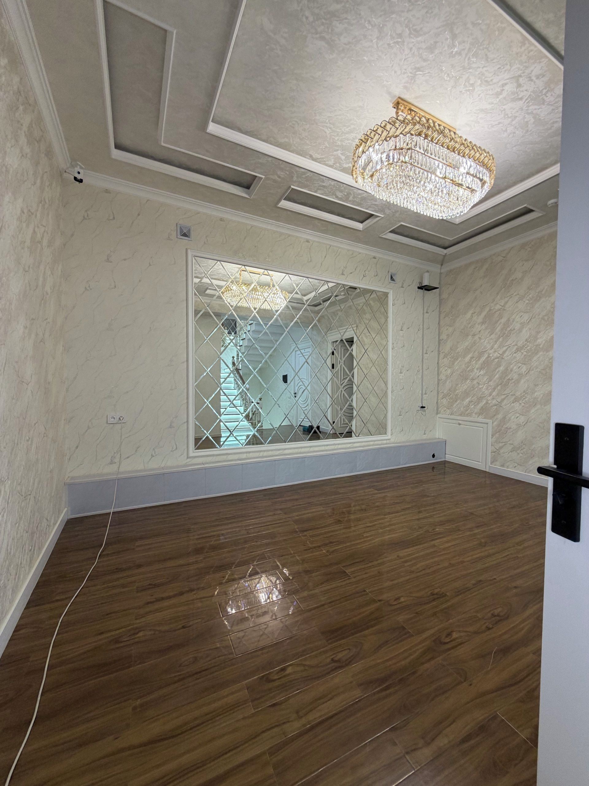 Una habitación con piso de madera, un candelabro y un amplio ventanal con diseño geométrico.