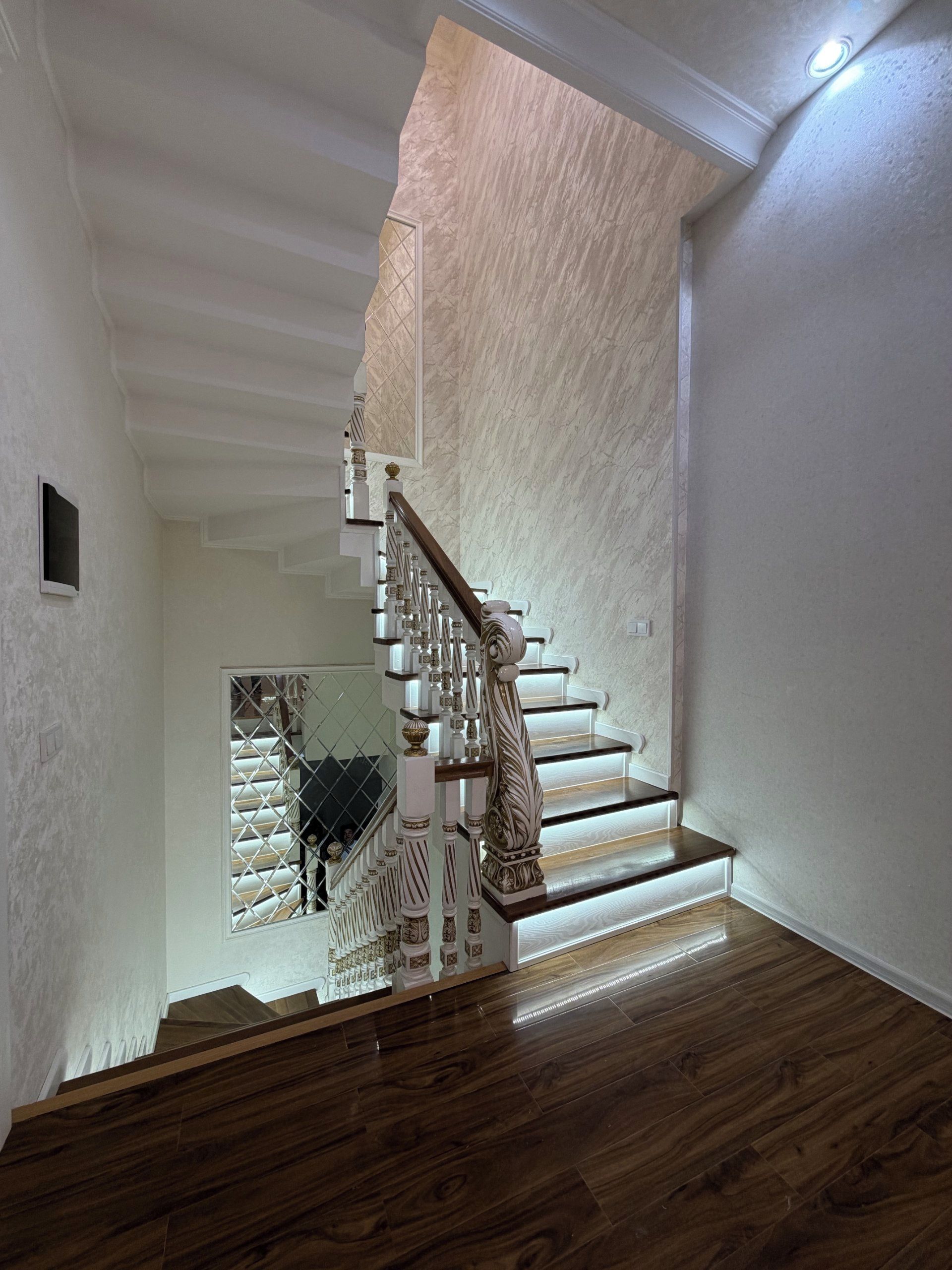 Una escalera con barandillas decorativas y una baranda de madera, que conduce a un rellano con una puerta de cristal.