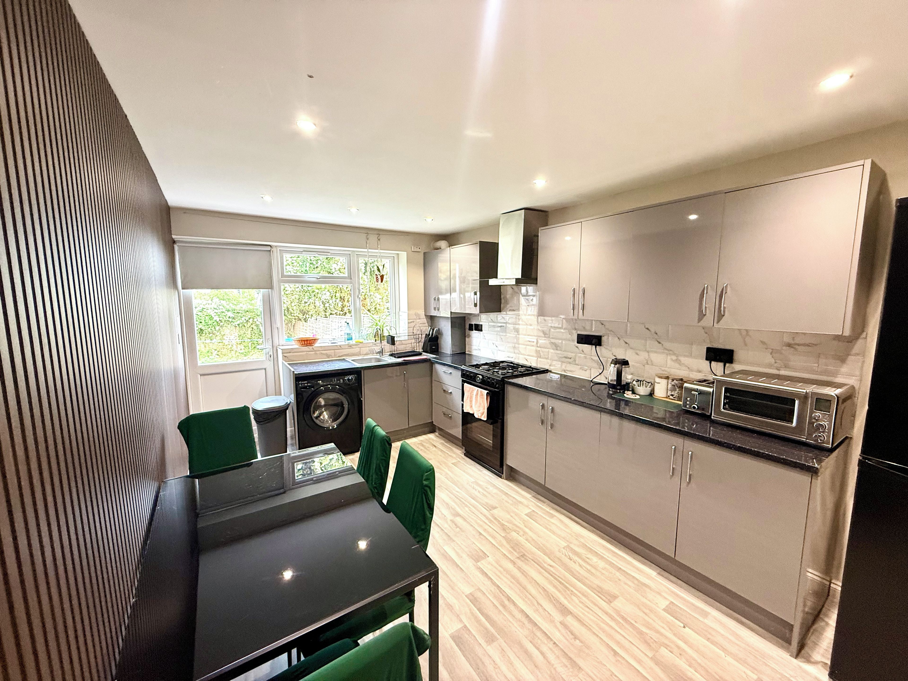 A modern kitchen with a dining area, built-in appliances, and a view of greenery outside.