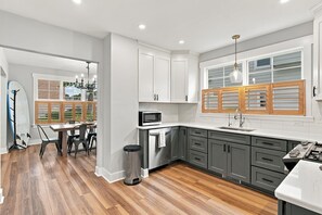 Une cuisine moderne avec des meubles blancs, un four à micro-ondes en acier inoxydable et une grande fenêtre dotée de volets en bois.