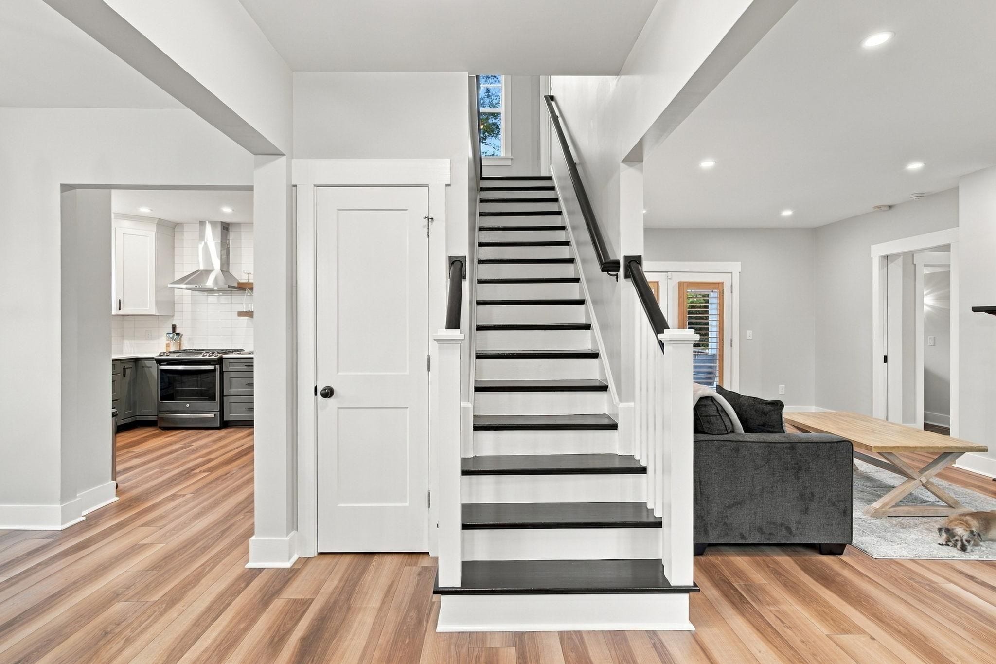 A modern interior with a staircase leading to a second floor, a kitchen area, and a seating area with a table and sofa.