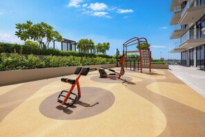 Ein Fitnessbereich im Freien mit Trainingsgeräten, umgeben von Grünflächen und modernen Gebäuden.