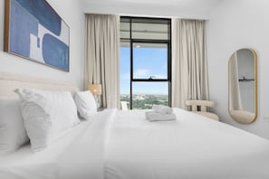 A hotel room with a large bed, a view through the window, and a painting on the wall. - StayShort - Refined Classy 1 Bedroom in Dubai Hills - Sleeps 2! (Dubai Hills)