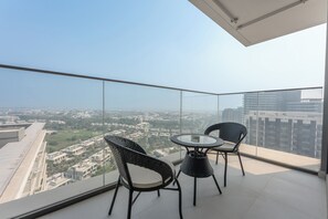 Ein Balkon mit Glasgeländer, zwei Korbstühle, ein kleiner runder Tisch und Blick auf die Stadt.