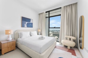 Een hotelkamer met een groot bed, een nachtkastje met een lamp, een stoel, een groot raam met gordijnen en uitzicht op de stad.