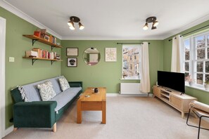 A living room with a green sofa, a wooden coffee table, a television, and bookshelves. - Town centre l 1bd apt l 5 min to station (Hertfordshire)