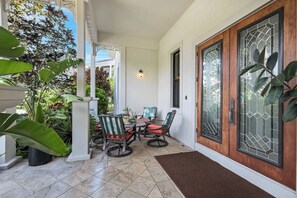 A covered patio area with a table and chairs, a wooden door with glass panels, and potted plants. - Hemingway Place - Charming Naples Retreat (Naples)
