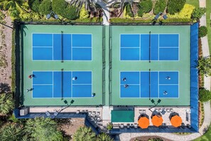 An aerial view of a tennis court complex with four courts, seating areas, and surrounding greenery. - Esplanade Golf & Country Club (Naples)