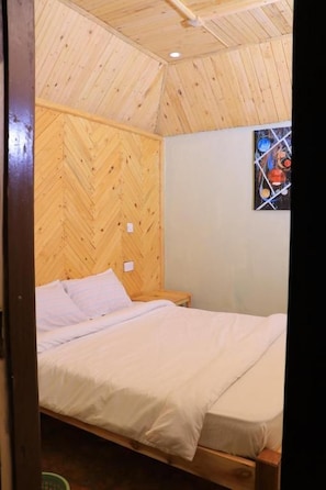 Una habitación con una cama, paredes de madera, un ventanal pequeño y un cuadro.