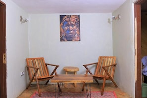 Um quarto pequeno com duas cadeiras de madeira, uma mesa redonda e um quadro na parede.