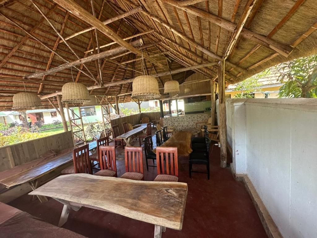 An outdoor dining area with wooden tables and chairs, a thatched roof, and hanging light fixtures.