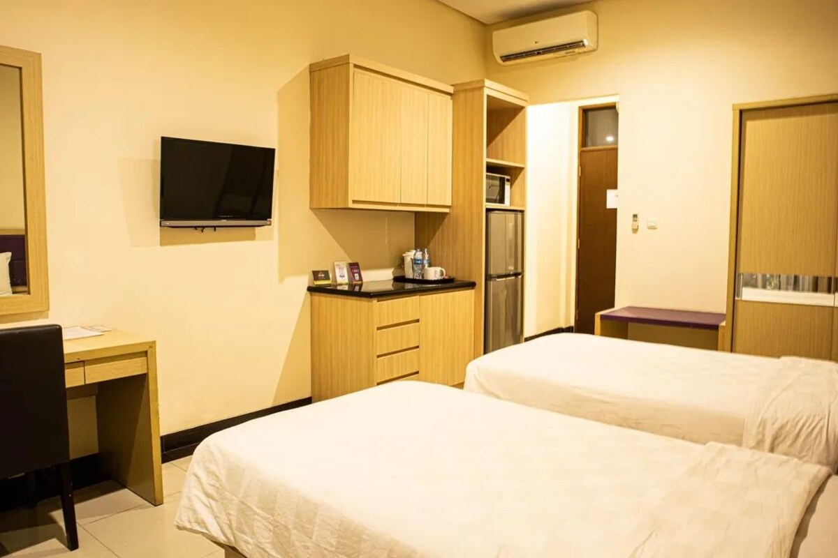 A hotel room with two beds, a desk, a TV, a kitchenette, and a wardrobe.