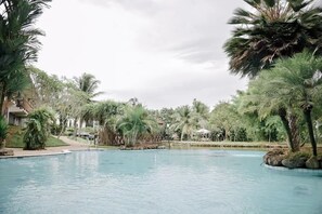 Ein Swimmingpool, umgeben von Palmen und viel Grün, mit Gebäuden im Hintergrund.