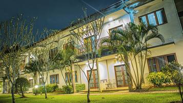 A multi-story hotel with a balcony on the second floor, surrounded by well-maintained lawns and various plants.